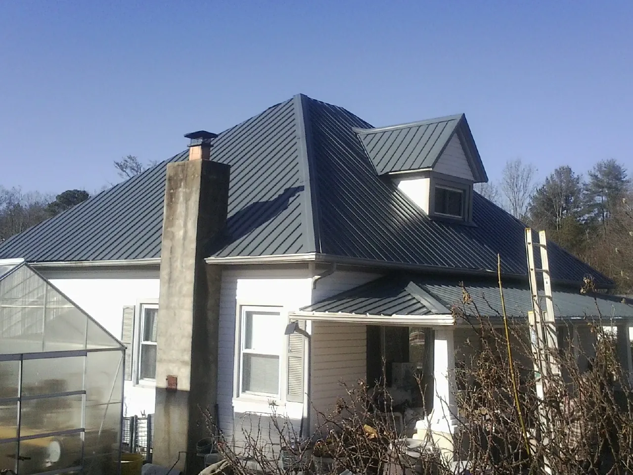 Dark blue standing seam metal roof on a white farmhouse with dormer — Slate & Tile Roof Repair by Roofing Brothers in Park Hills