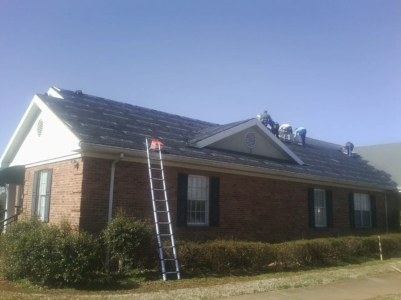 Crew tearing shingles off a brick ranch roof with a ladder set — Emergency Roof Repair work by our crew in Park Hills