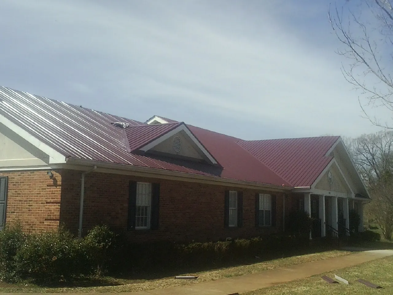 Red metal roof with gabled entries on a long brick building, from a Hail Damage Roof Repair job in Park Hills