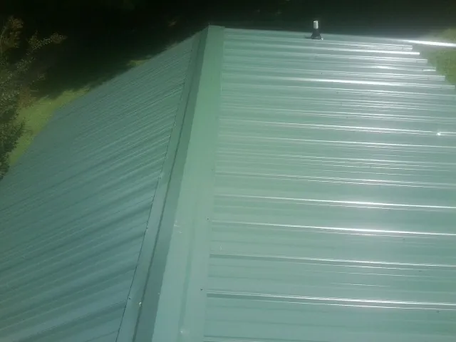 New green metal panels meeting at the ridge of a roof — Flat Roof Repair work by our crew in Park Hills