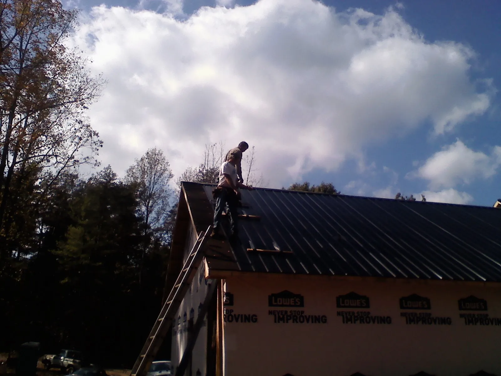 Roofer fastening dark metal panels high against a cloudy sky, from a Roof Inspection job in Park Hills