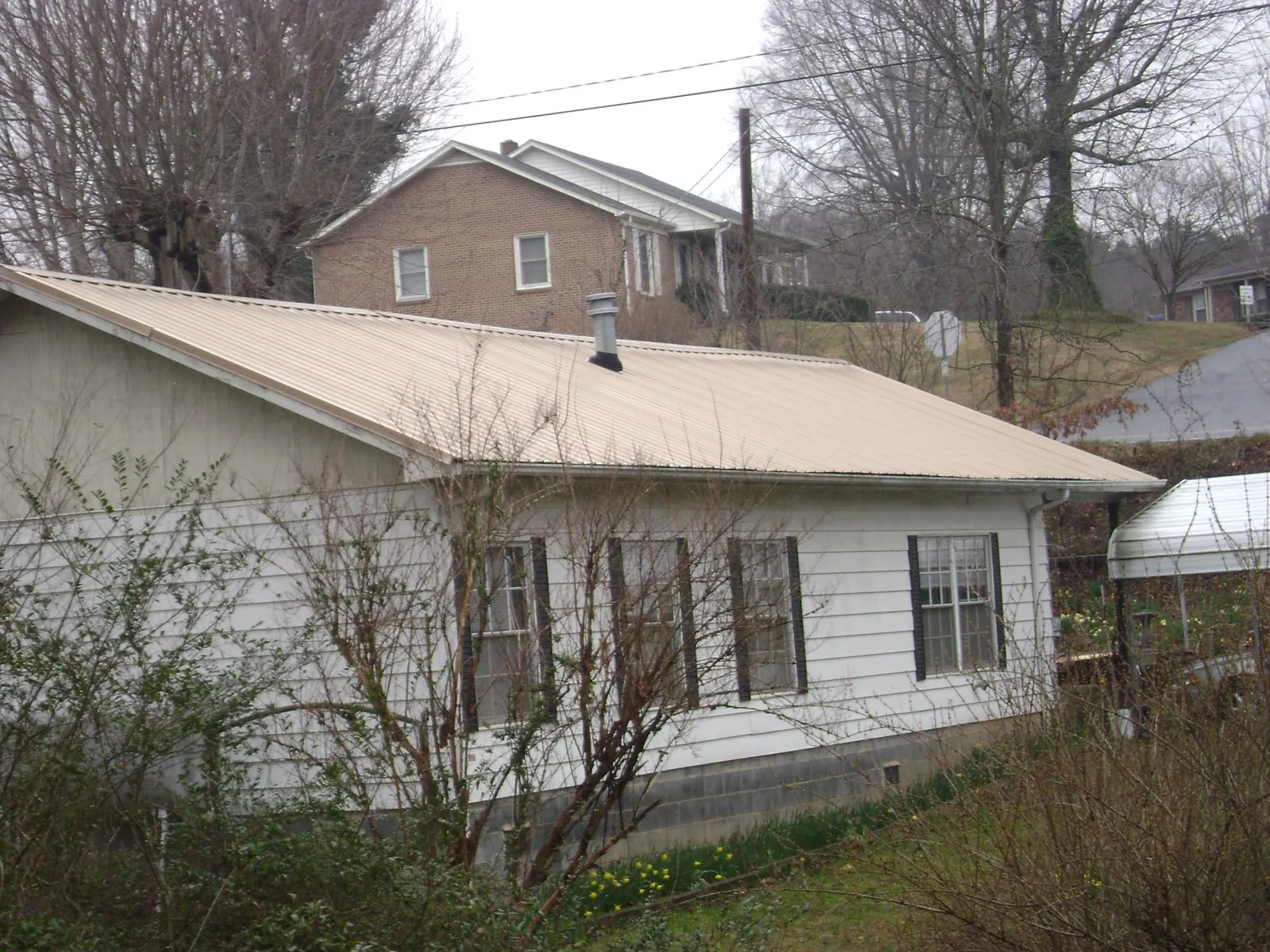 Tan metal roof on a white sided house set into a hillside — Commercial Roofing by Roofing Brothers in Park Hills