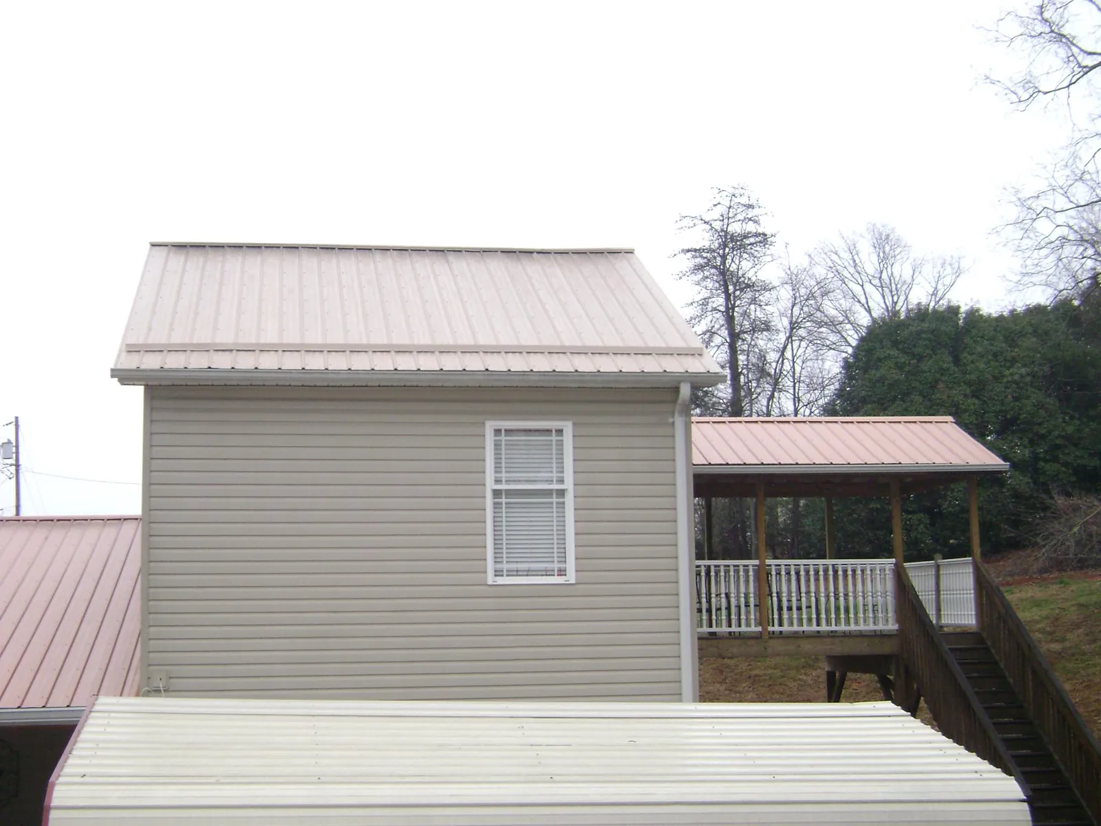 Tan metal roofs on a two story addition and attached porch, from a Roof Replacement job in Park Hills